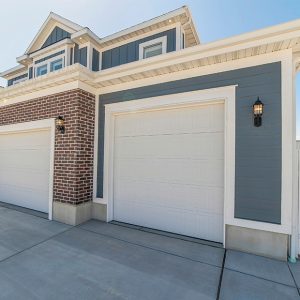 A home with lap and brick siding has white garage doors.