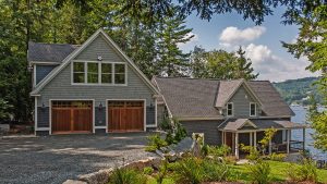 A beautiful grey lake house with a wood two-stall garage.