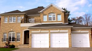 A large house with stone siding has three whit garage doors.
