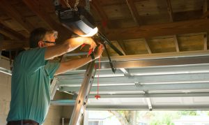 A technician standing on a ladder repairing a garage door opener